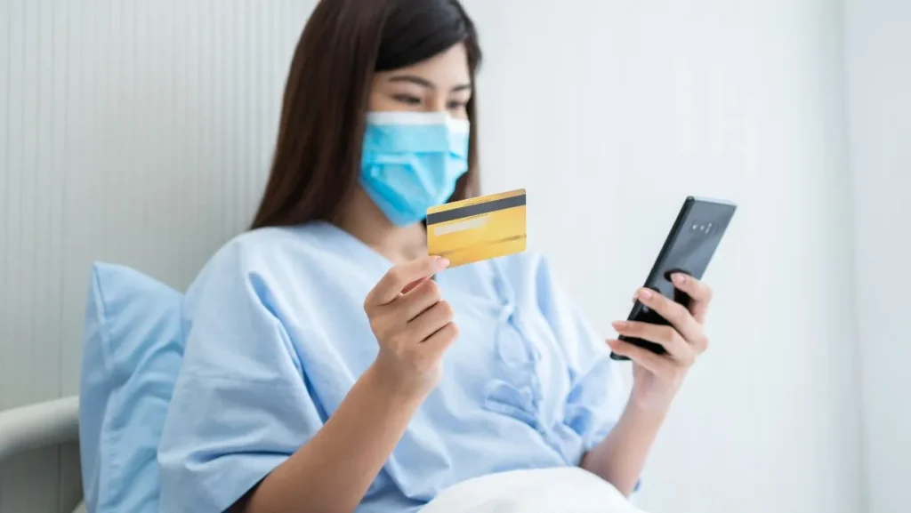 Happy Asian Woman Wearing A Medical Mask And Holding Mock Up Credit Insurance Card And Smartphone 1024x577