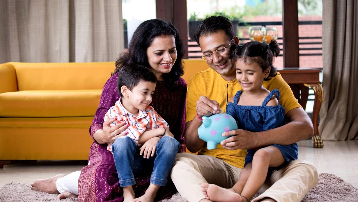 Parents With Children Saving Money In Piggy Bank